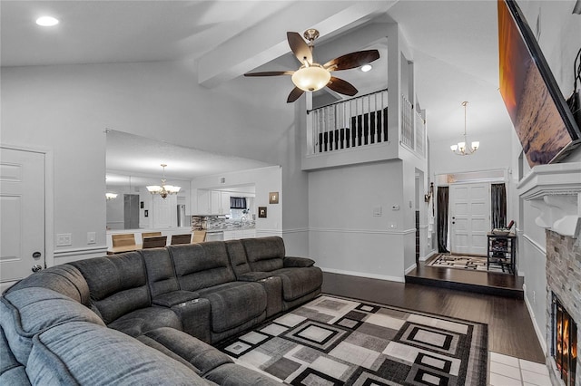 living room featuring beam ceiling, high vaulted ceiling, hardwood / wood-style floors, a fireplace, and ceiling fan with notable chandelier