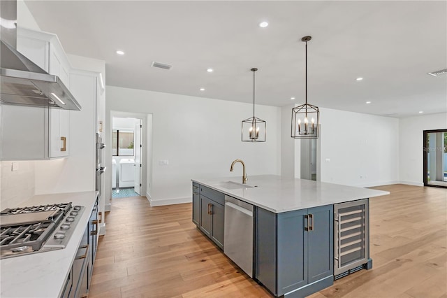 kitchen featuring hanging light fixtures, appliances with stainless steel finishes, wall chimney exhaust hood, sink, and white cabinets