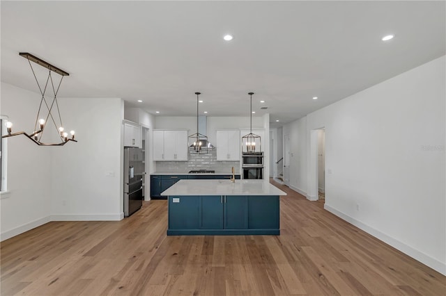 kitchen with hanging light fixtures, white cabinetry, tasteful backsplash, an island with sink, and an inviting chandelier