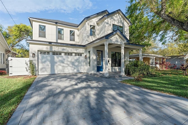 modern farmhouse style home featuring stucco siding, driveway, a gate, a front yard, and an attached garage