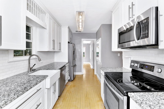 kitchen featuring light stone countertops, stainless steel appliances, white cabinets, and light wood-type flooring