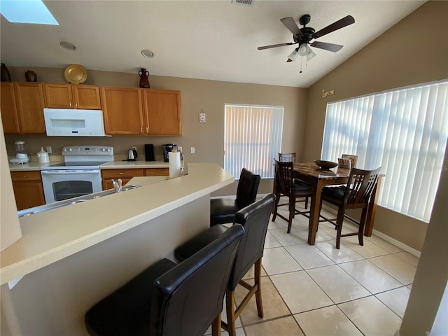 kitchen with ceiling fan, light tile patterned floors, white appliances, vaulted ceiling with skylight, and a breakfast bar area