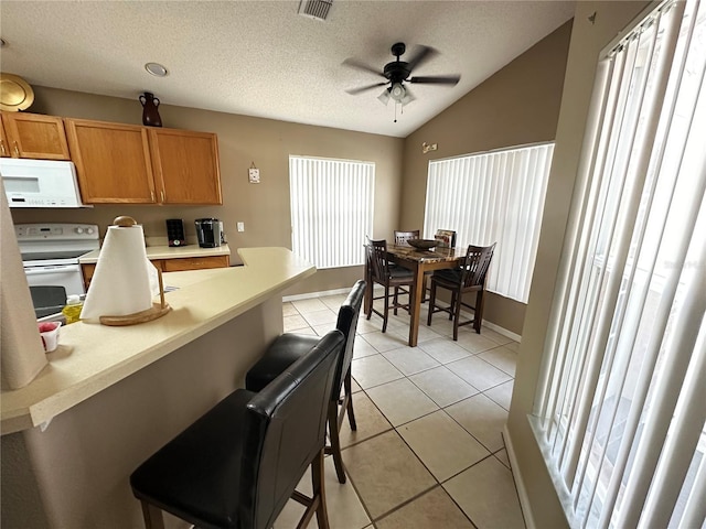 kitchen with white appliances, lofted ceiling, ceiling fan, light tile patterned floors, and a breakfast bar area