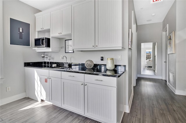 kitchen featuring sink, wood-type flooring, dark stone counters, and white cabinets