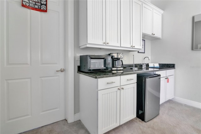 kitchen with white cabinetry, sink, light carpet, and stainless steel refrigerator