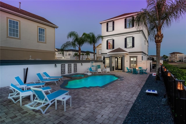 pool at dusk featuring an in ground hot tub and a patio area