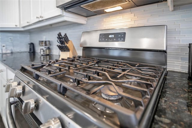 details with white cabinetry, wall chimney range hood, gas stove, and dark stone countertops