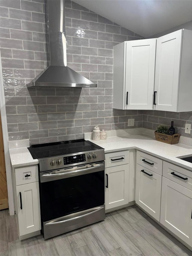 kitchen featuring white cabinets, stainless steel range with electric stovetop, vaulted ceiling, and wall chimney range hood