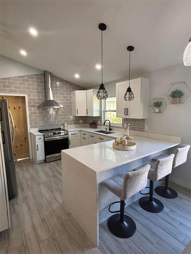 kitchen with white cabinets, appliances with stainless steel finishes, kitchen peninsula, and wall chimney range hood