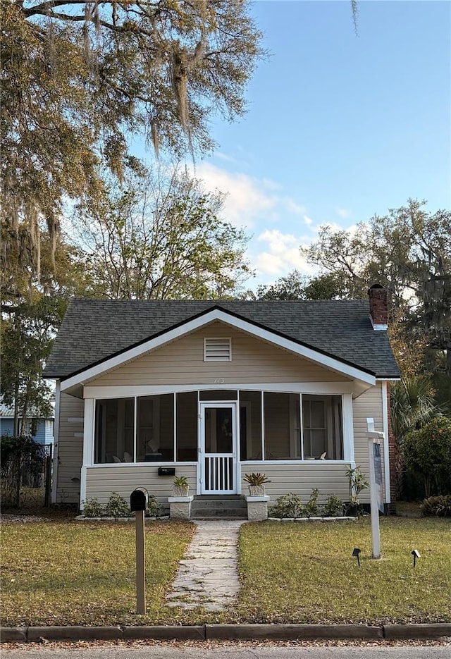 bungalow-style house with a front yard, a sunroom, roof with shingles, and a chimney