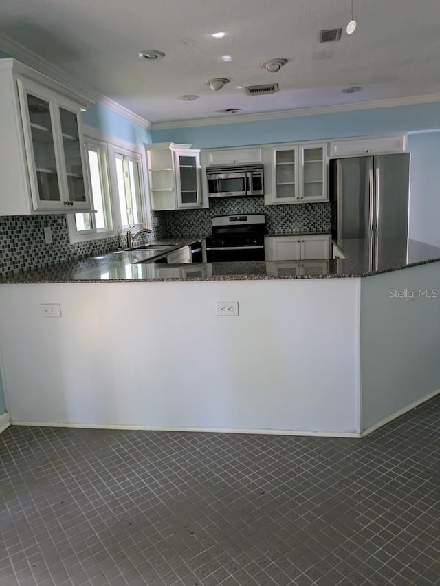 kitchen featuring appliances with stainless steel finishes, white cabinetry, dark stone countertops, ornamental molding, and kitchen peninsula