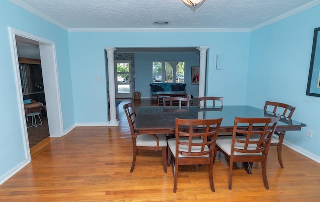 dining area featuring decorative columns, ornamental molding, and light wood-type flooring