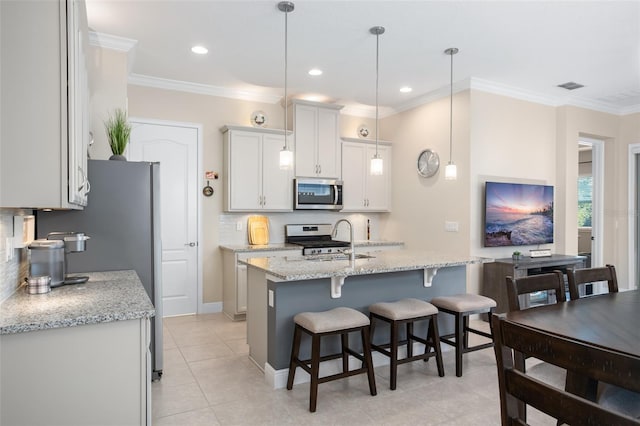 kitchen featuring pendant lighting, stainless steel appliances, a center island with sink, and white cabinets