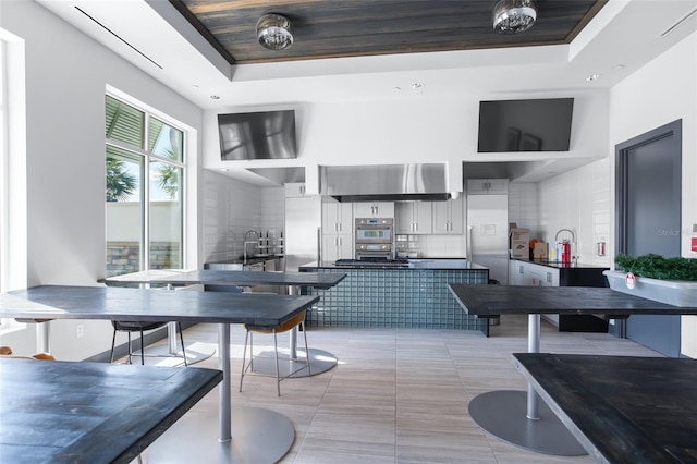 kitchen featuring light tile patterned floors, a high ceiling, tasteful backsplash, a raised ceiling, and stainless steel double oven