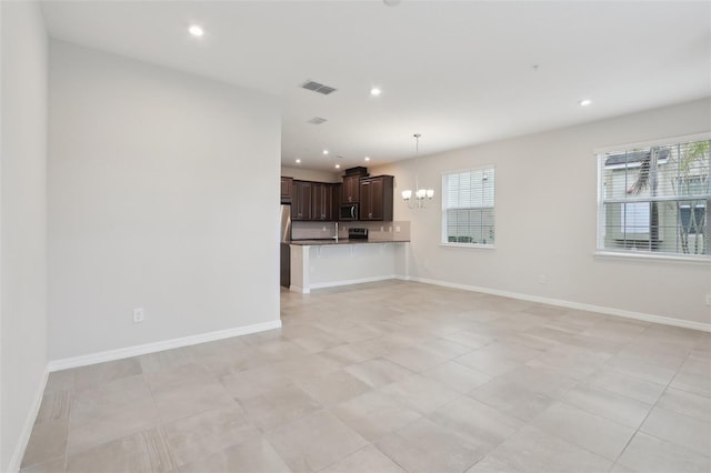 unfurnished living room with light tile patterned flooring, a chandelier, and a healthy amount of sunlight