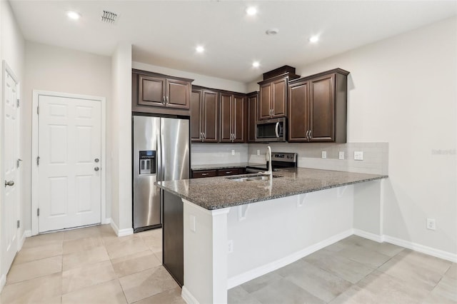 kitchen featuring stainless steel appliances, dark stone countertops, sink, a kitchen breakfast bar, and kitchen peninsula