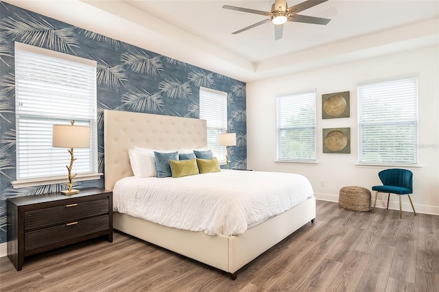 bedroom with ceiling fan, wood-type flooring, and a raised ceiling