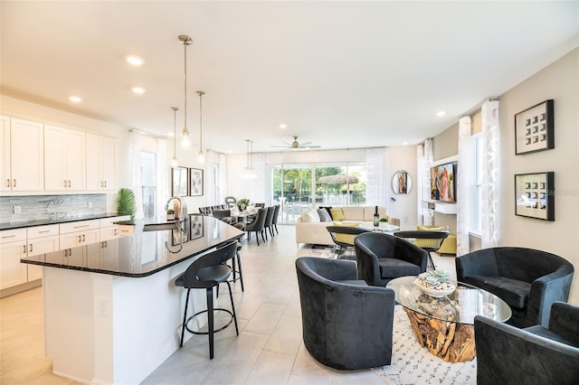 kitchen with decorative backsplash, a kitchen breakfast bar, white cabinets, pendant lighting, and an island with sink