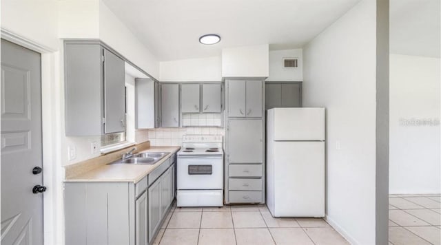 kitchen featuring sink, tasteful backsplash, light tile patterned floors, gray cabinets, and white appliances