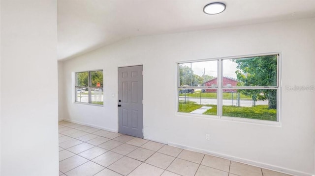 unfurnished room with a healthy amount of sunlight, light tile patterned floors, and lofted ceiling