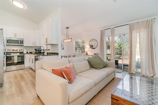 living room with lofted ceiling, sink, an inviting chandelier, and light hardwood / wood-style flooring