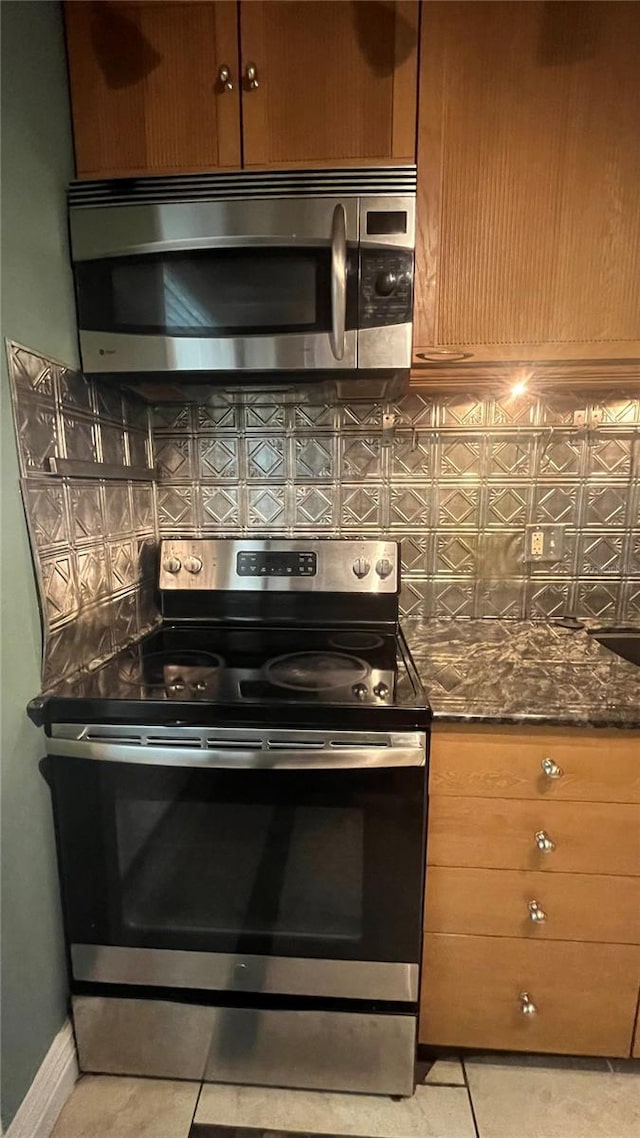 kitchen with appliances with stainless steel finishes, light tile patterned floors, backsplash, and dark stone counters