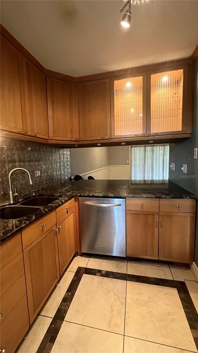 kitchen featuring sink, dark stone countertops, backsplash, stainless steel dishwasher, and light tile patterned floors