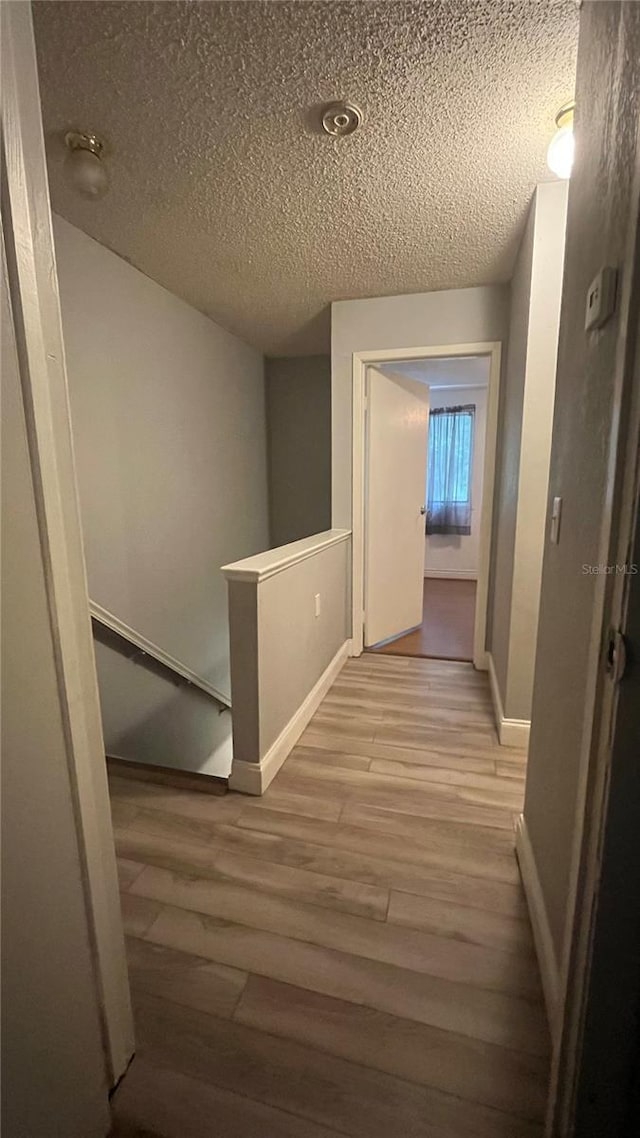 hallway with light hardwood / wood-style floors and a textured ceiling