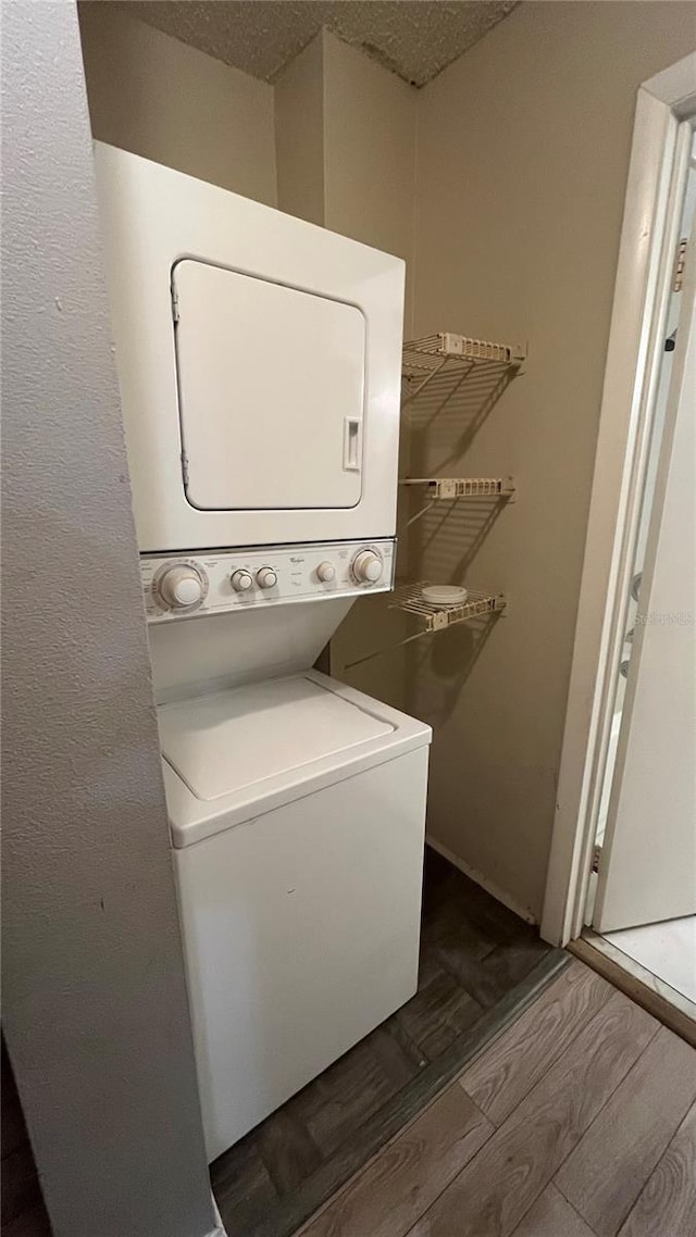 laundry area with dark wood-type flooring, a textured ceiling, and stacked washing maching and dryer