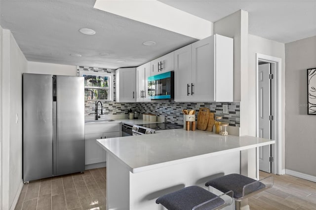 kitchen featuring white cabinetry, sink, kitchen peninsula, stainless steel appliances, and a breakfast bar area