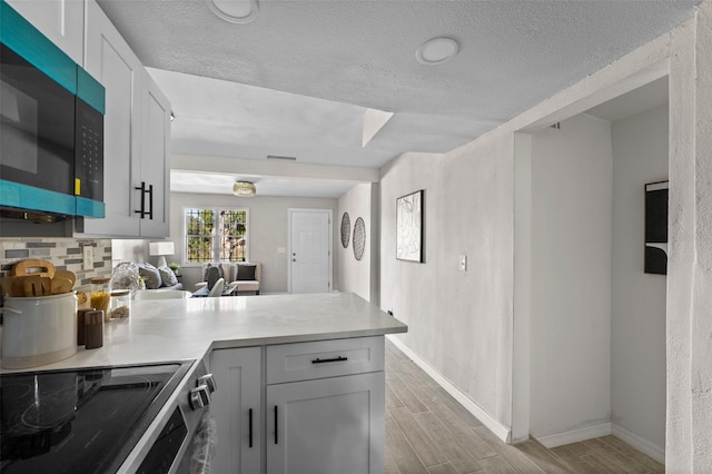 kitchen with kitchen peninsula, backsplash, white cabinetry, a textured ceiling, and stainless steel electric range