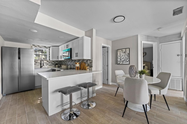 kitchen with kitchen peninsula, sink, backsplash, white cabinets, and stainless steel appliances