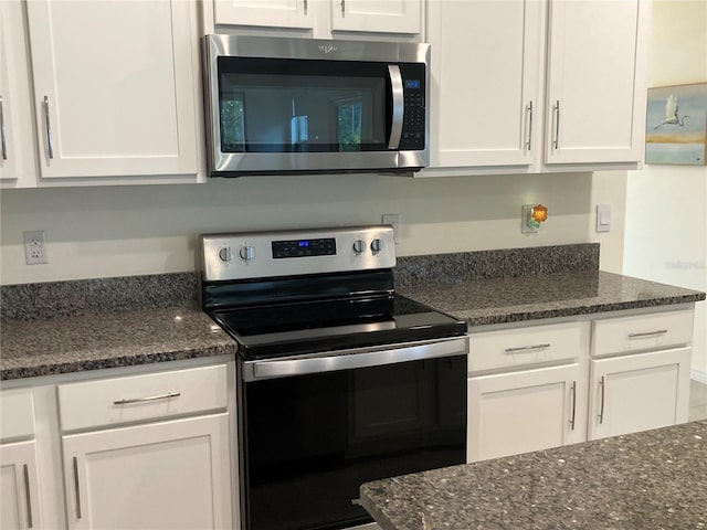 kitchen with stainless steel appliances, dark stone counters, and white cabinets