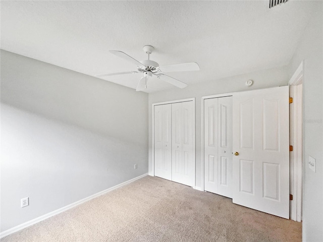 unfurnished bedroom featuring ceiling fan, two closets, and carpet flooring