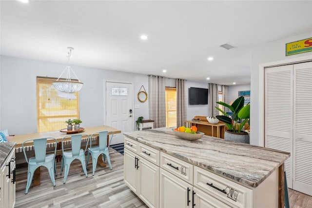 kitchen featuring light hardwood / wood-style floors, light stone countertops, pendant lighting, and a center island