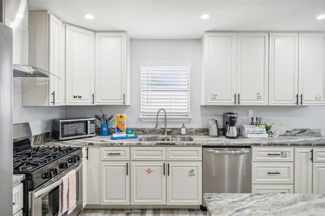 kitchen featuring wall chimney range hood, white cabinets, appliances with stainless steel finishes, and sink