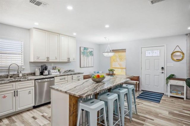 kitchen featuring dishwasher, sink, white cabinetry, light stone countertops, and a kitchen island