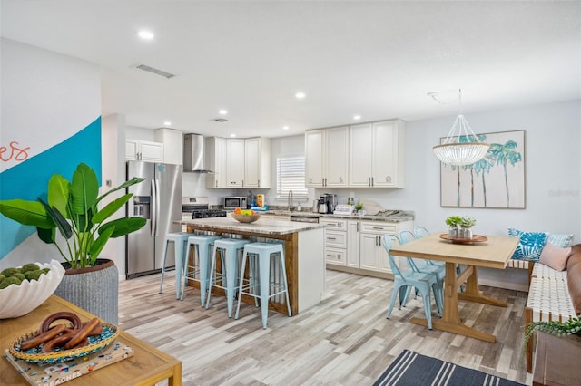 kitchen with white cabinetry, a kitchen island, pendant lighting, stainless steel appliances, and wall chimney exhaust hood