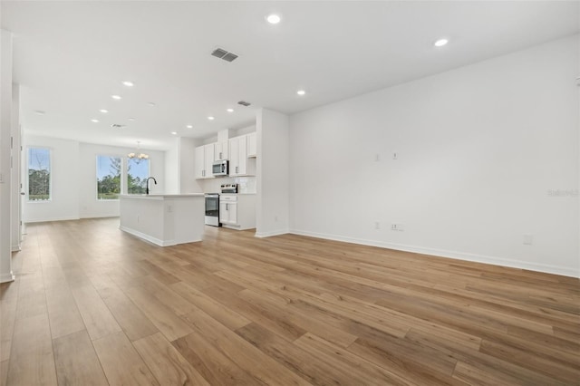 unfurnished living room featuring sink, an inviting chandelier, and light wood-type flooring