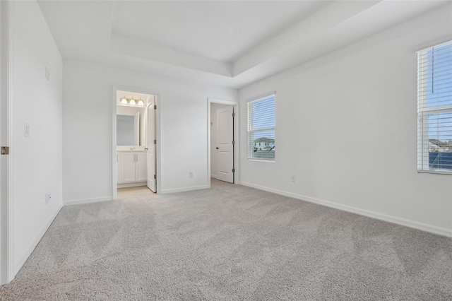 unfurnished bedroom featuring multiple windows, ensuite bath, light colored carpet, and a raised ceiling