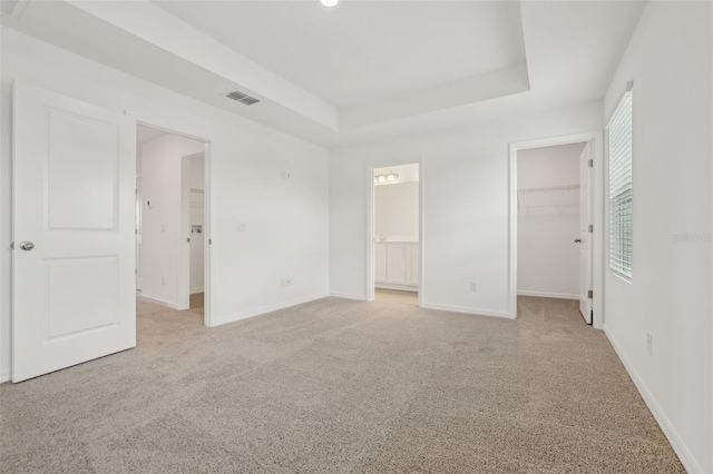 unfurnished bedroom with connected bathroom, a walk in closet, light colored carpet, a raised ceiling, and a closet