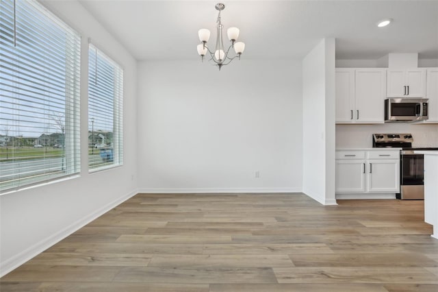 interior space featuring decorative light fixtures, light hardwood / wood-style flooring, stainless steel appliances, and white cabinets