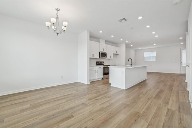 kitchen featuring appliances with stainless steel finishes, decorative light fixtures, sink, white cabinets, and a kitchen island with sink