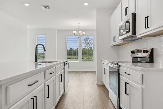 kitchen with sink, light hardwood / wood-style flooring, hanging light fixtures, appliances with stainless steel finishes, and white cabinets