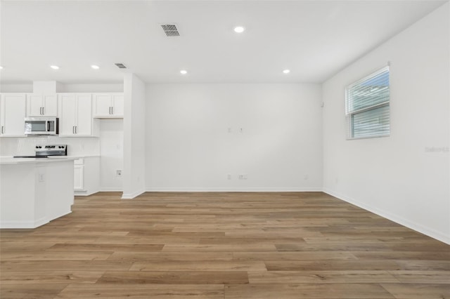 kitchen with backsplash, stainless steel appliances, light wood-type flooring, and white cabinets