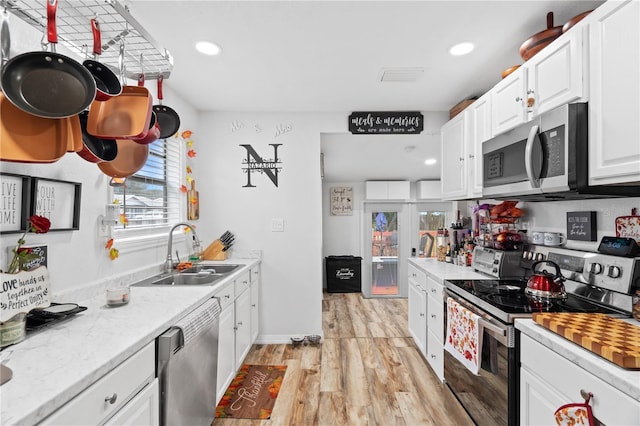 kitchen featuring sink, appliances with stainless steel finishes, white cabinetry, light stone countertops, and light wood-type flooring