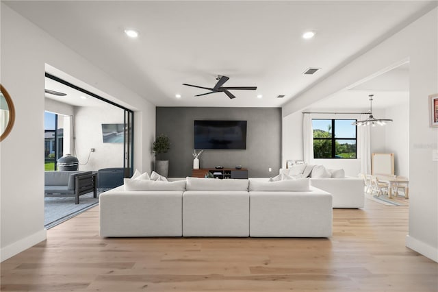 living room with ceiling fan with notable chandelier and light hardwood / wood-style flooring