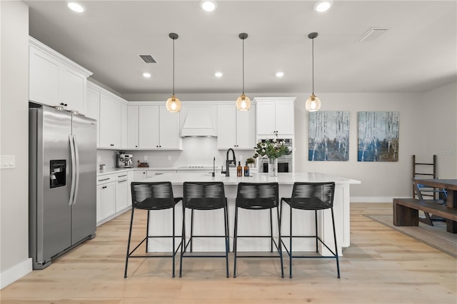 kitchen with premium range hood, white cabinets, stainless steel fridge with ice dispenser, and a kitchen island with sink