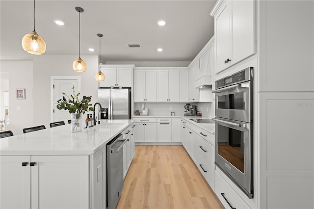 kitchen featuring stainless steel appliances, white cabinetry, pendant lighting, and an island with sink