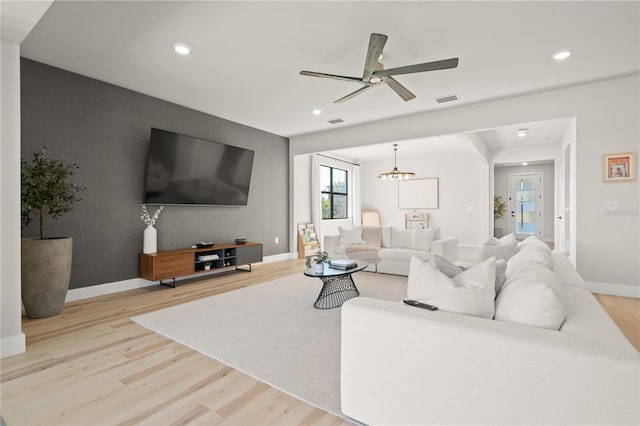 living room with ceiling fan with notable chandelier and light hardwood / wood-style floors